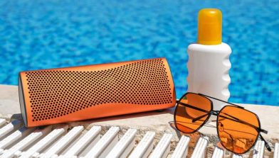 orange-coloured-beach-accessories-near-swimming-pool-sun-cream-sunglasses-music-bluetooth-speaker-min